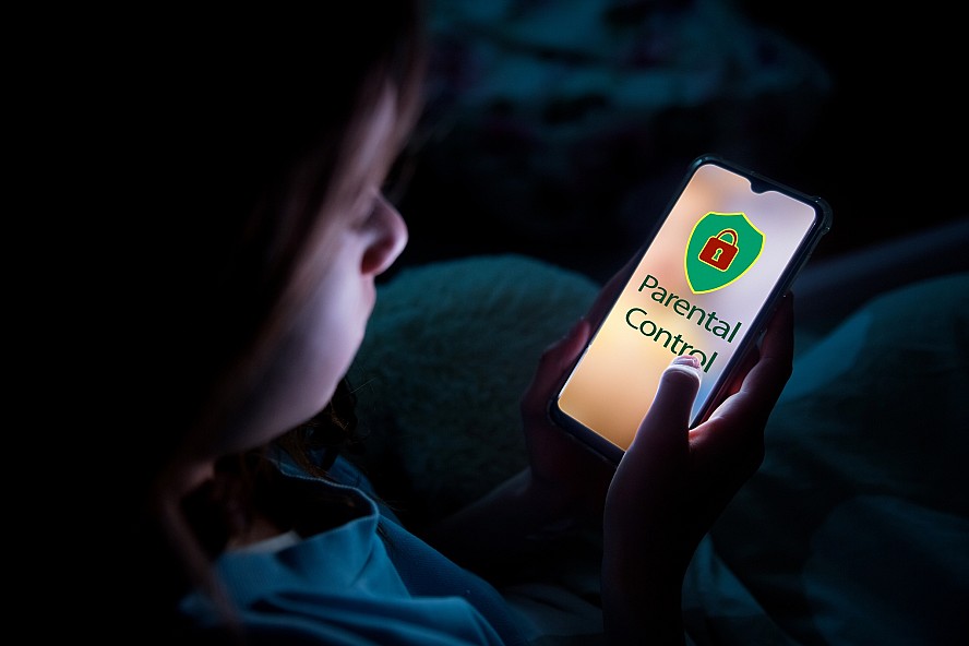 young child in a dark room looking at a lighted smartphone screen that says 